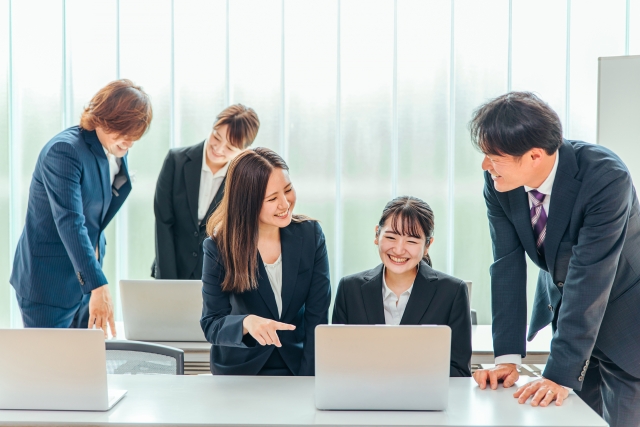 オフィスでパソコンを覗き込みながらグループワークするスーツの人々
