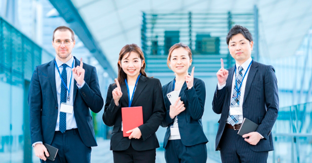 人差し指を立ててこちらを見る四人のビジネスパーソン