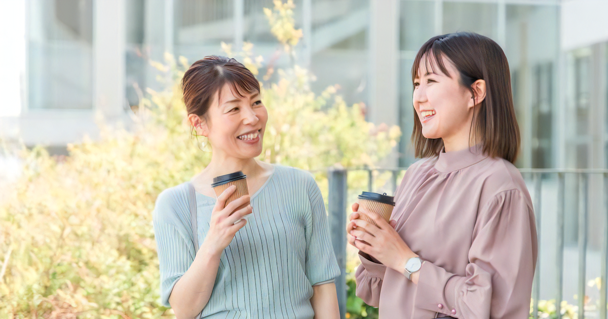 テイクアウトのコーヒーを手に談笑する女性二人