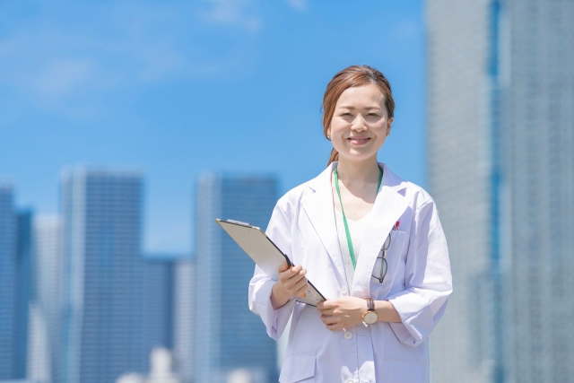 高層ビル群を背景に笑顔で佇む女性医師
